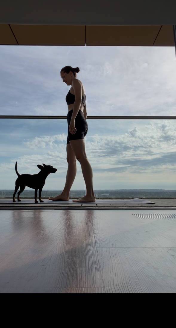 Olga standing on a yoga mat by large studio windows